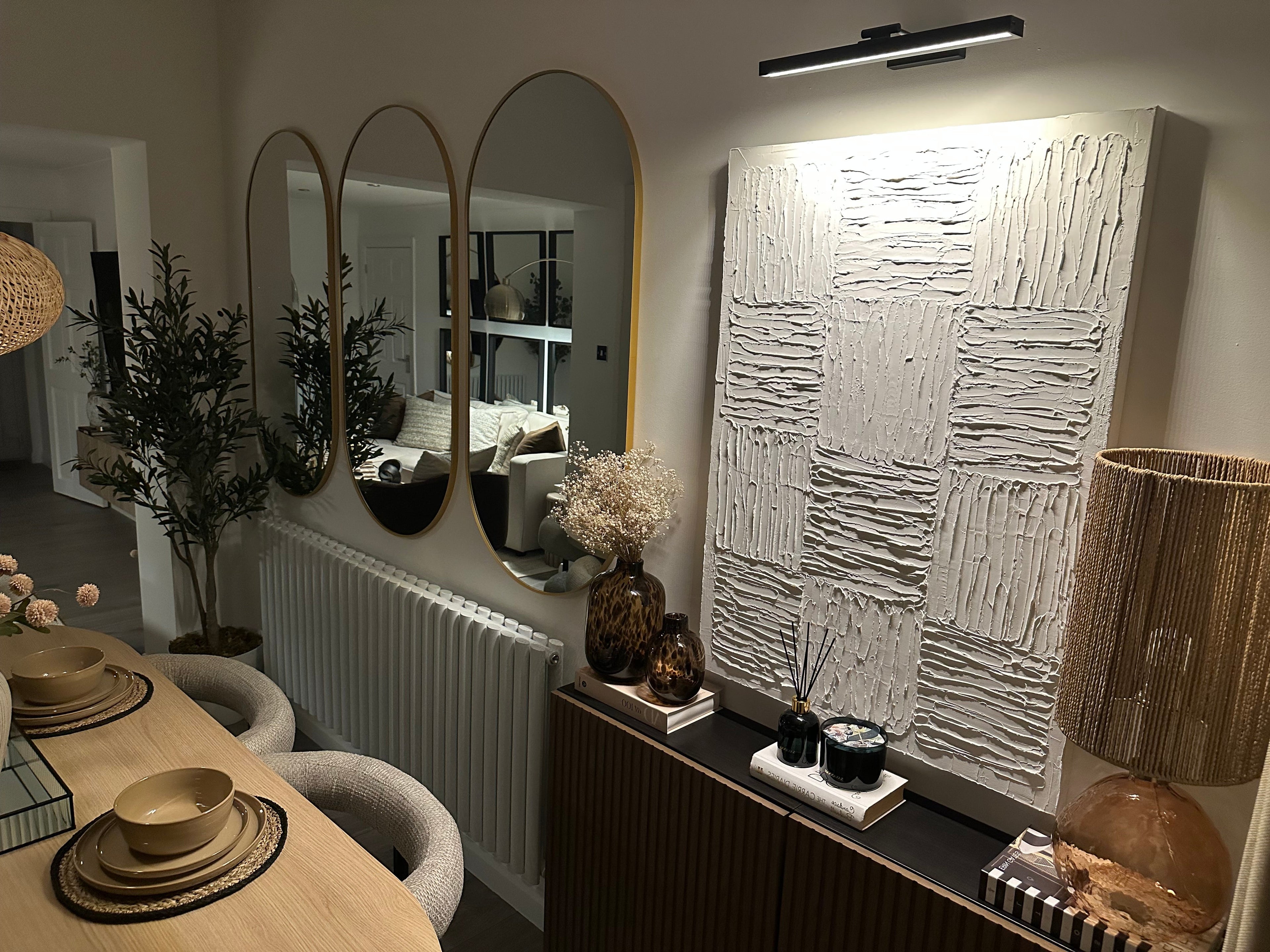 Modern interior design with textured wall art, mirrors, and a dining table setup.